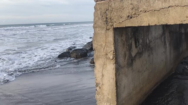 Water dripping from coastal rock on a rocky beach with crashing ocean waves, concept of coastal erosion, climate change, and sea level rise.