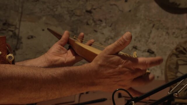 The master crafts traditional wooden string instruments by hand. The traditional musical instrument is the Calabrian lyre. The master works in the cozy light of his workbench.