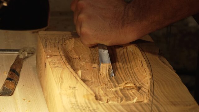 The master crafts traditional wooden string instruments by hand. The traditional musical instrument is the Calabrian lyre. The master works in the cozy light of his workbench.
