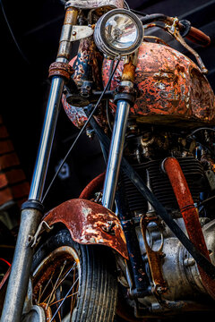 Detailed close up of an antique rusty motorcycle featuring corroded fuel tank, classic round headlight, and vintage mechanical engine