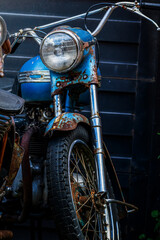 Fototapeta premium Vintage Rusted Blue Motorcycle Front View Close-Up with Classic Round Headlight and Chrome Handlebars in Dark Garage Setting