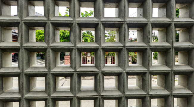 Concrete breeze block wall, geometric square pattern with green trees and street view through perforated architectural screen texture