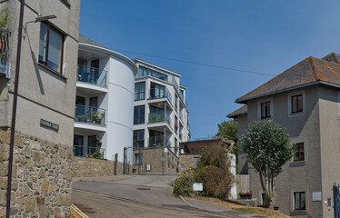 Fototapeta premium A sunny street scene showing modern buildings on the left, traditional homes on the right, and a paved road leading uphill - Penzance, Cornwall, UK