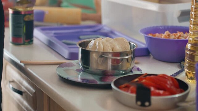 Close-up kitchen workspace with metal sifter holding pressed ingredient on digital scale beside bowl of sliced red peppers and clear containers, showing careful prep, organized tools, and subtle