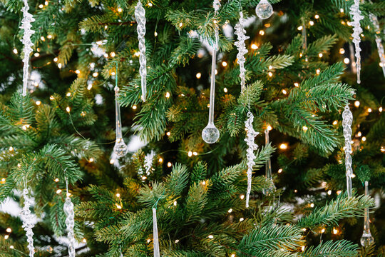 Christmas tree branch decorated with clear glass ornaments, glass icicle decorations and warm glowing lights, elegant festive background with winter atmosphere. Holiday mood, aesthetic decor