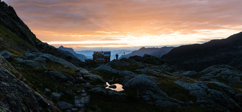 Bergh&uuml;tte in den Tiroler Alpen bei Sonnenaufgang mit spiegelndem Bergsee, dramatischem Morgenhimmel und schroffen Gipfeln in alpiner Hochgebirgslandschaft