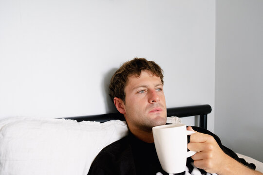 UGC Man holding coffee in bed with thoughtful morning expression