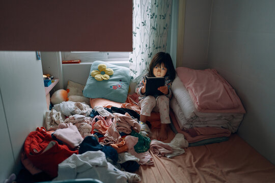 Child using a tablet on a Messy Bedroom 