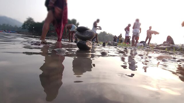 Defocused Sacred River Bathing at Devghat Dham, Nepal, with Balanced River Stones in Foreground, Hindu Pilgrimage, Spiritual Ritual, Peaceful Riverside Landscape and Cultural Heritage