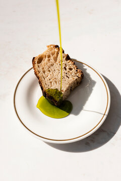 Pouring vibrant green olive oil onto a slice of sourdough bread