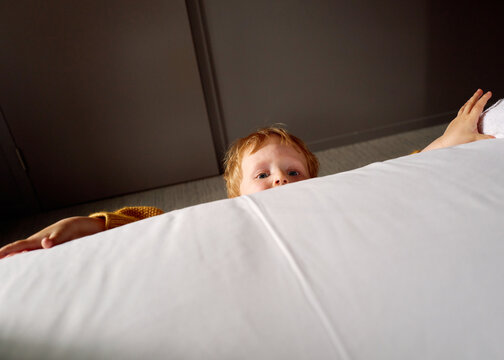 Child Peeking Over White Bedspread in a Dimly Lit Room