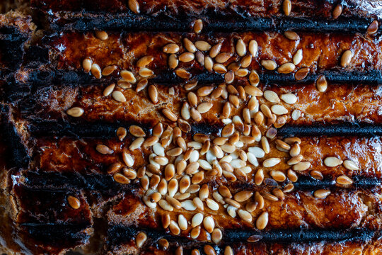 Closeup macro texture of baked bun crust with sesame seeds. Macro shot of dark golden brown grilled or baked pastry crust sprinkled with toasted white sesame seeds showing charred stripes texture