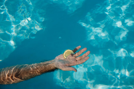 Hand Holding Lemon Slice Above Swimming Pool Water