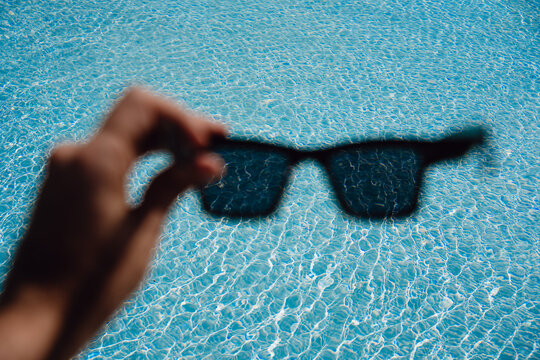 Holding Sunglasses Above Clear Swimming Pool Water