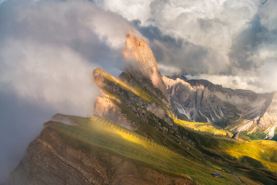 Seceda mountain peak with dramatic fog and clouds at sunset in Dolomites, Italy. Alpine summer landscape with cliff edge, sunbeams, green grass slope, high rocks, sunlight and valley. Aerial view
