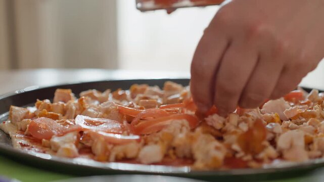 Close-up low-angle view of hands actively placing cooked shrimp and tails on shallow round serving dish, showing plating motion with suspended shrimp and fingers mid-gesture