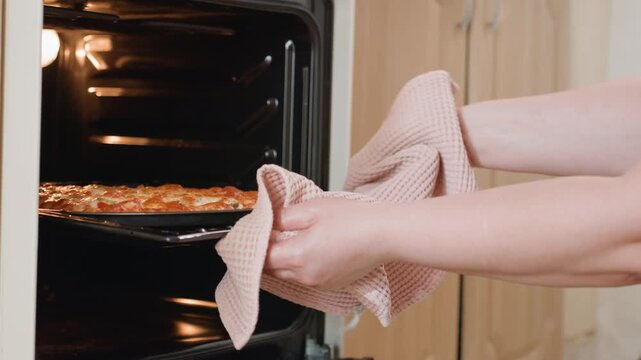 Close-up of hands wearing textured mitts pulling browned baking tray from built in oven, showing careful removal of hot dish, steady outward motion, warm kitchen light, and safe home cooking
