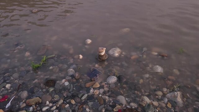 Defocused Sacred River Bathing at Devghat Dham, Nepal, with Balanced River Stones in Foreground, Hindu Pilgrimage, Spiritual Ritual, Peaceful Riverside Landscape and Cultural Heritage