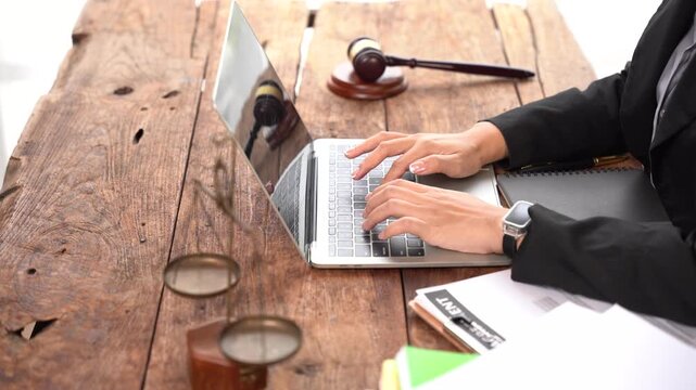Justice at Work: A legal professional meticulously types on a laptop, surrounded by essential courtroom paraphernalia such as a gavel and a magnifying glass.