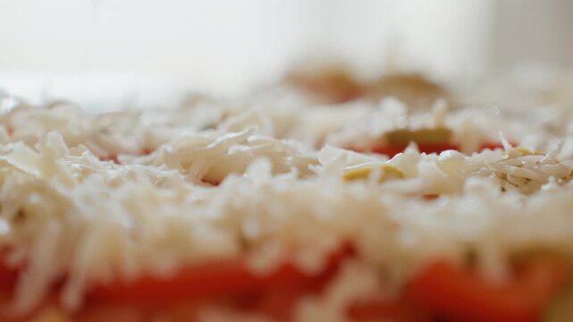 Low-angle close view showing shredded white cheese falling onto sliced tomatoes and mixed salad ingredients, creating layered topping with textured strands, fresh color, and appetizing food detail