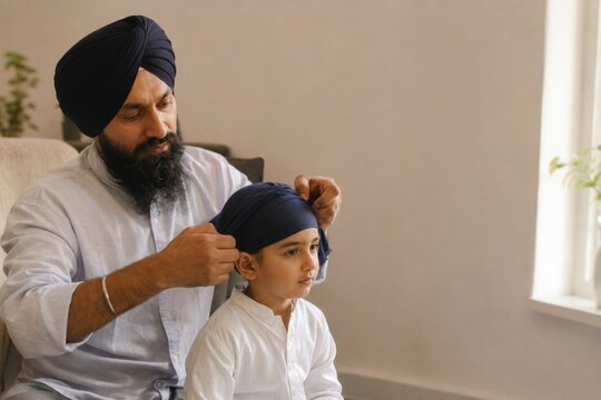 Sikh father carefully tying a turban on his child at home. Family tradition, cultural heritage, parenting, religious identity, and intergenerational bonding concept with copy space.