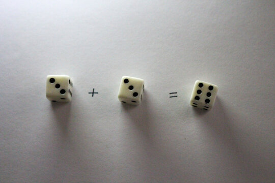 An addition math problem shows white dice &mdash; displaying numbers via their dots &mdash; on a white background, casting shadows. three plus three equals six