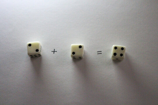 An addition math problem shows white dice&mdash;displaying numbers An addition math problem shows white dice&mdash;displaying numbvia their dots&mdash;on a white background, casting shadows. two plus two equals four 