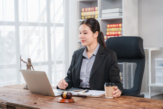 Lawyer Working on Laptop: A female lawyer in a professional suit sits at her desk, holding a coffee cup and working on a laptop. A gavel and law books are visible in the background.