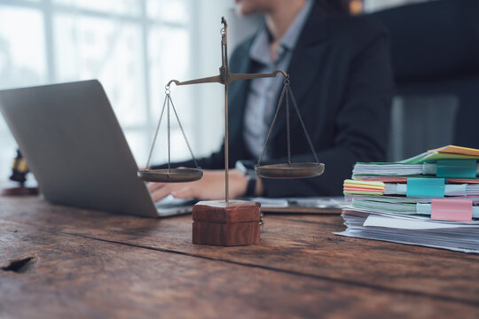 Justice on the Desk: A law professional works diligently at a wooden desk, with a laptop, stacks of documents, and a traditional justice scale symbolizing fairness and legal proceedings.