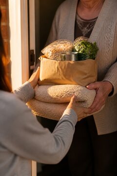 Woman receiving a care package with groceries and warm blankets at home. Community support, food donation, neighborly kindness, and assistance for vulnerable people during winter.