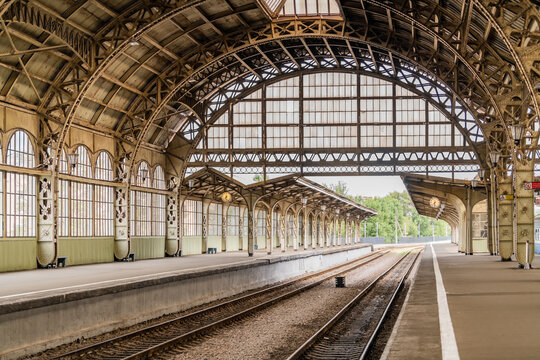 Historic railway station platform with ornate iron arches, glass roof, clocks, and empty train tracks. Architectural heritage and public transport travel concept.