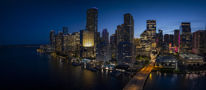Aerial view of the illuminated Brickell skyline at night with skyscrapers reflecting on the water and city lights in Miami, Florida, United States.