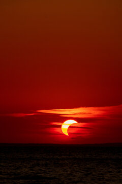 solar eclipse over the adraitic sea, seen from croatian coast, on august, 12th, 2026, during the golden hour as the sun was setting partially covered  with a moon with few colorful clouds on red sky 