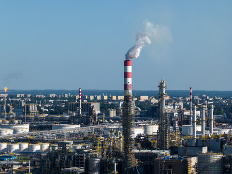 Aerial view of the PKN Orlen refinery complex with tall chimneys emitting smoke, storage tanks, and intricate pipe networks in Plock, Masovian Voivodeship, Poland.