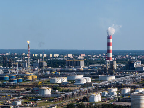 Aerial view of PKN Orlen oil refinery with a tall red and white chimney emitting smoke, storage tanks, and industrial infrastructure in Plock, Masovian Voivodeship, Poland.