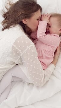 A mother hugging and playing with her little girl on the bed at home, joyful family moment, cozy lifestyle, happy childhood.