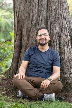 Happy man sitting cross legged by large tree trunk in park