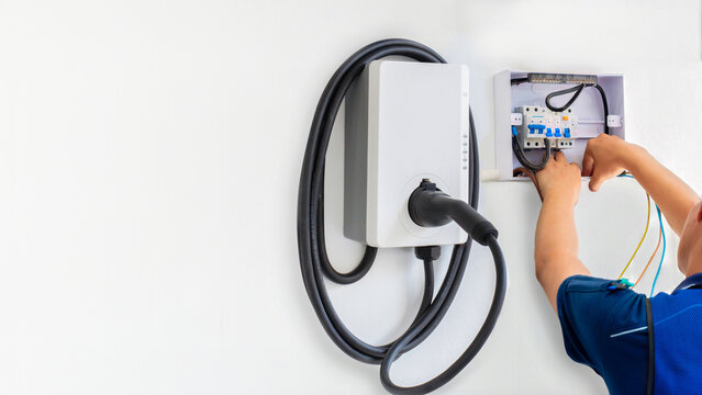 Electrician installing EV wall box charger and residential breaker panel on white wall for home electric vehicle charging station energy infrastructure setup and maintenance