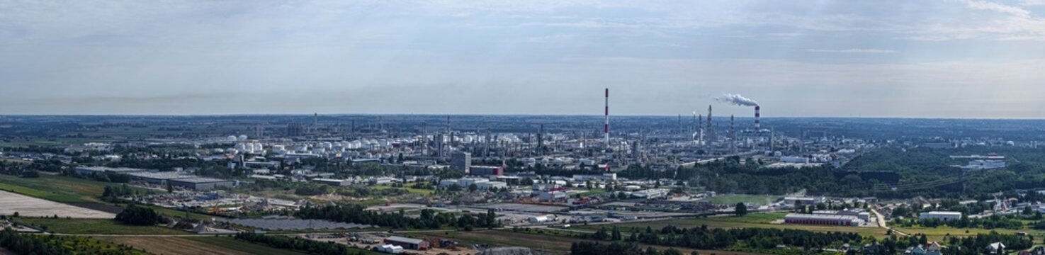 Aerial view of the extensive PKN Orlen refinery complex featuring industrial towers, storage tanks, and smoking chimneys surrounded by green fields, Plock, Masovian Voivodeship, Poland.