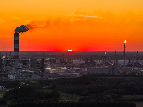 Aerial view of the PKN Orlen oil refinery with industrial chimneys and flare stacks silhouetted against a vibrant sunset sky in Plock, Masovian Voivodeship, Poland.