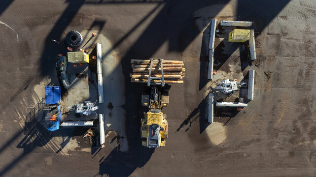 Aerial view of a yellow log loader transporting timber in an industrial yard with concrete barriers and equipment in Nelson, Nelson Region, New Zealand.