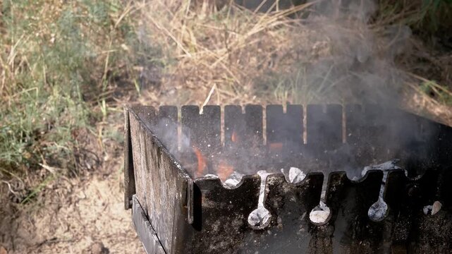 Thick smoke rises from burning coals inside an outdoor metal barbecue grill set up on the grass. Concept of outdoor cooking, summer picnic, traditional barbecue, and weekend leisure.