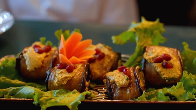 Traditional georgian badrijani nigvzit, delicious eggplant rolls stuffed with walnut paste and herbs, garnished with fresh pomegranate seeds and served on a bed of lettuce leaves in a restaurant