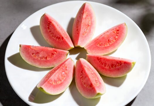 Slices of fresh pink guava arranged on a white plate with vitamin c tropical vegetarian top-view