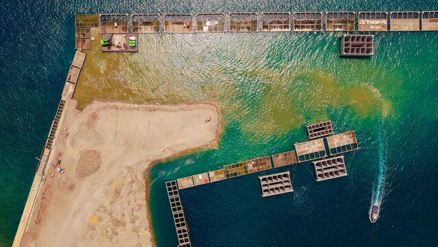 Aerial view of Piraeus Harbour showing industrial construction, concrete structures in the water, and a small boat navigating the turquoise sea in Athens, Greece.
