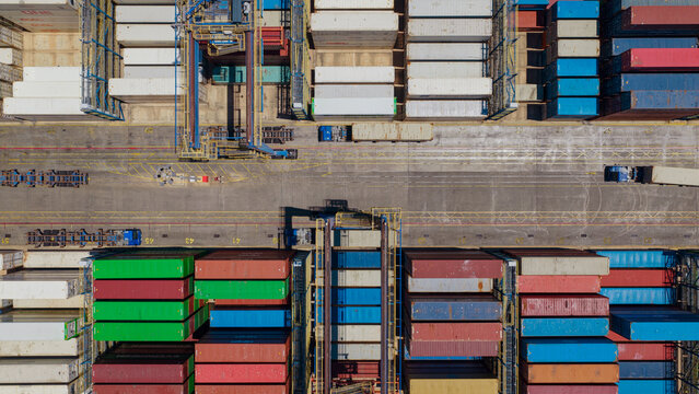 Aerial view of Piraeus Harbour featuring rows of colorful shipping containers stacked in the terminal with industrial cranes and transport vehicles in Athens, Greece.