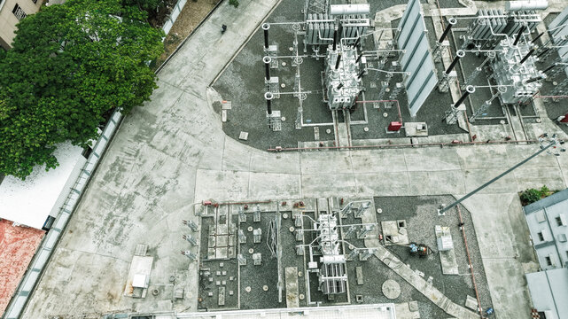 Aerial view of the Tharamani electrical substation featuring industrial transformers, switchgear, and gravel grounds surrounded by a large tree in Chennai, Tamil Nadu, India.