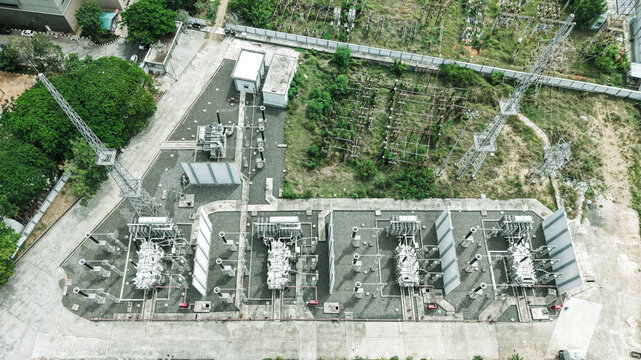 Aerial view of Tharamani electrical substation with large transformers, power transmission towers, and metal infrastructure in a gravel-covered industrial site in Chennai, Tamil Nadu, India.