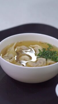 Slow motion camera panning of traditional uzbek chuchvara dumpling soup served with fresh herbs and sour cream, vertical video.