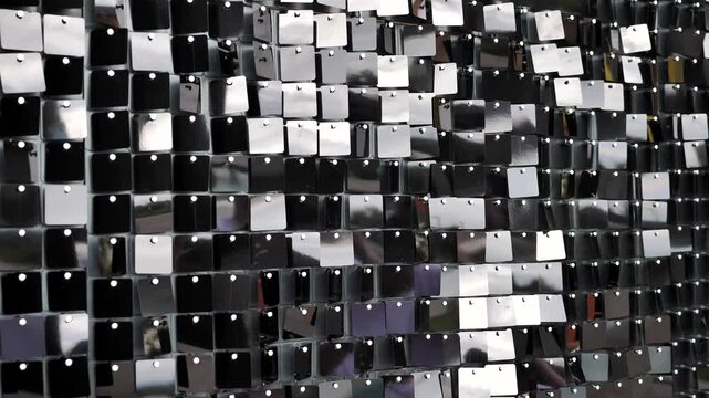 A modern kinetic photo booth made from small, square, black, glossy sequins that capture dynamic light reflections and create a luxurious, dark, abstract texture.